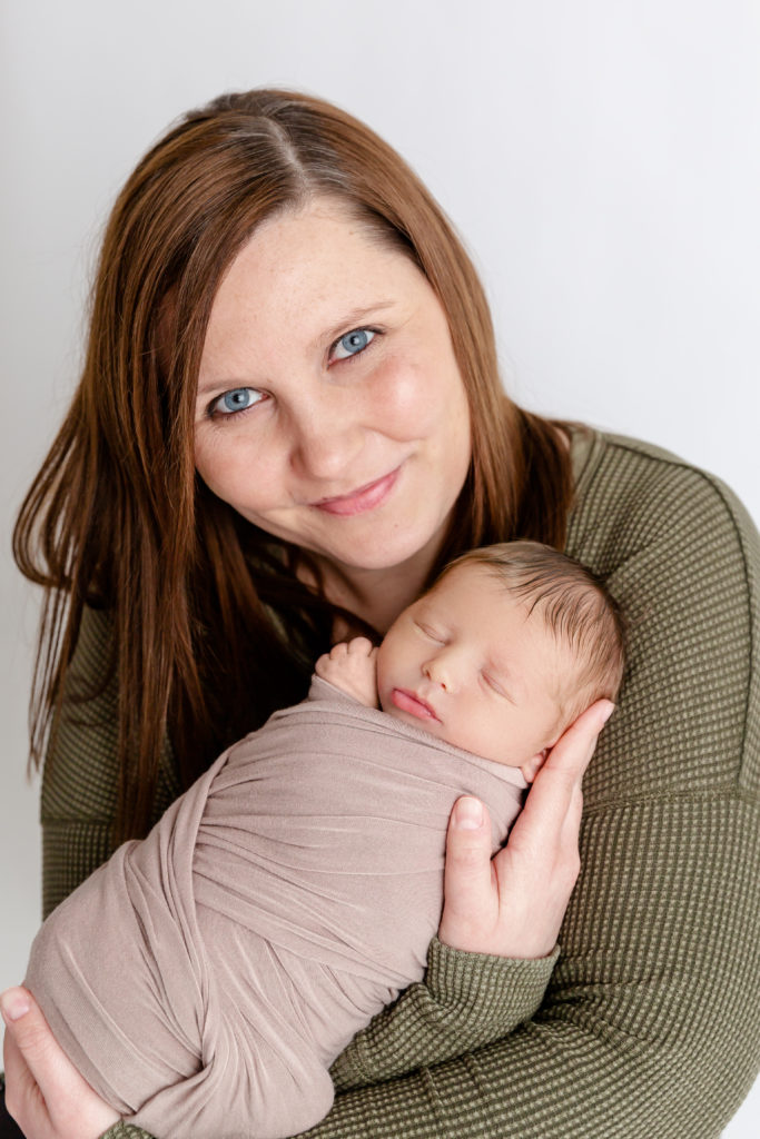Newborn boy wrapped in swaddle photographed with mom for newborn portrait session