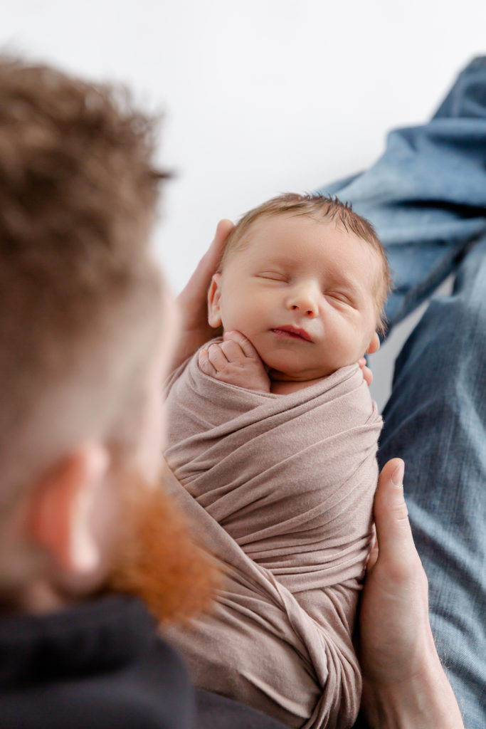 Newborn boy wrapped in swaddle photographed with dad for newborn portrait session