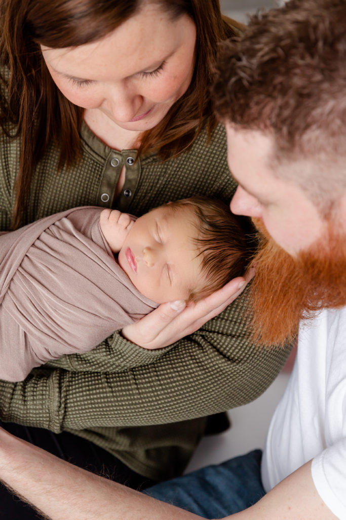 Newborn boy wrapped in swaddle photographed with parents for newborn portrait session